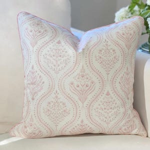 May include: A square throw pillow featuring a cream-colored fabric with a repeating dusty pink botanical pattern. The design consists of vertical ogee-shaped panels filled with intricate floral and leaf motifs, finished with matching pink piping.