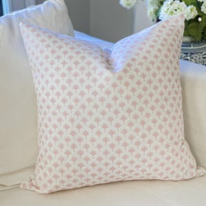 May include: A square throw pillow featuring a repeating pattern of small, light pink fan-shaped motifs printed on a solid white fabric background. The pillow has a clean, structured shape with visible seams along the edges and a soft, plush appearance.