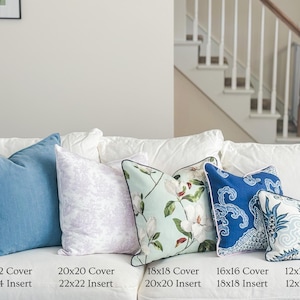 May include: A collection of decorative throw pillows in various sizes and designs, including solid blue, floral, and patterned options. Sizes range from 12x20 inches to 22x22 inches. The pillows are arranged on a white sofa, offering a range of textures and colors.