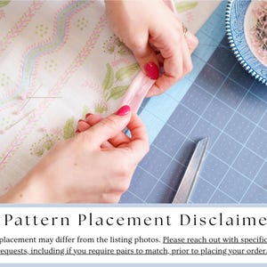 May include: A close-up of hands working with fabric and sewing supplies. The hands are holding a pink ribbon, with a pair of scissors and a blue and white bowl of pins nearby. The fabric has a floral pattern. The image includes the text "Pattern Placement Disclaimer".
