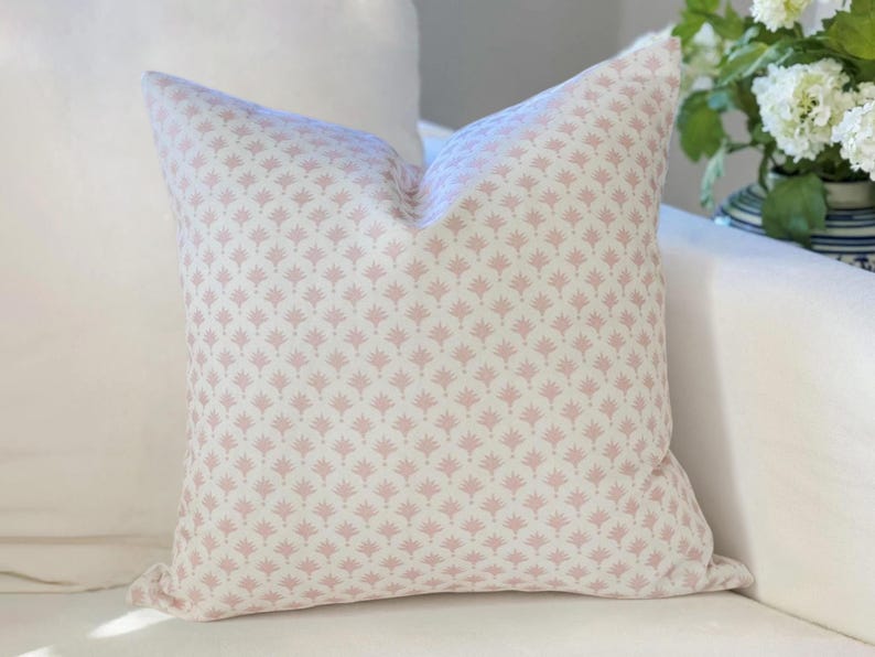 May include: A square throw pillow featuring a repeating pattern of small, dusty pink fan-shaped motifs printed on a cream-colored fabric background. The pillow has a soft, plump appearance with clean, straight edges and a consistent, symmetrical design.