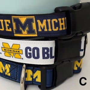 May include: Three blue and yellow dog collars with the text "Go Blue" and "Michigan" on them. The collars are attached to a black buckle.