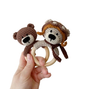 Puede incluir: Un mordedor de madera para beb&eacute; con dos ositos de peluche de crochet unidos. Un oso lleva una bufanda marr&oacute;n y un gorro marr&oacute;n y naranja.