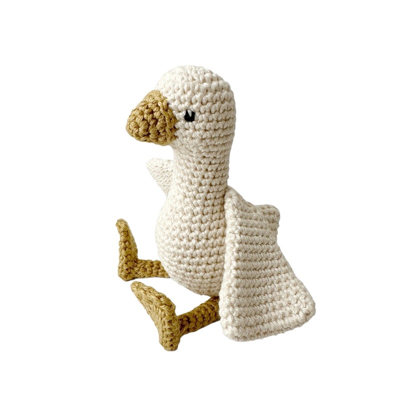May include: A crocheted goose toy with white and tan yarn. The goose has a small black eye and a tan beak.