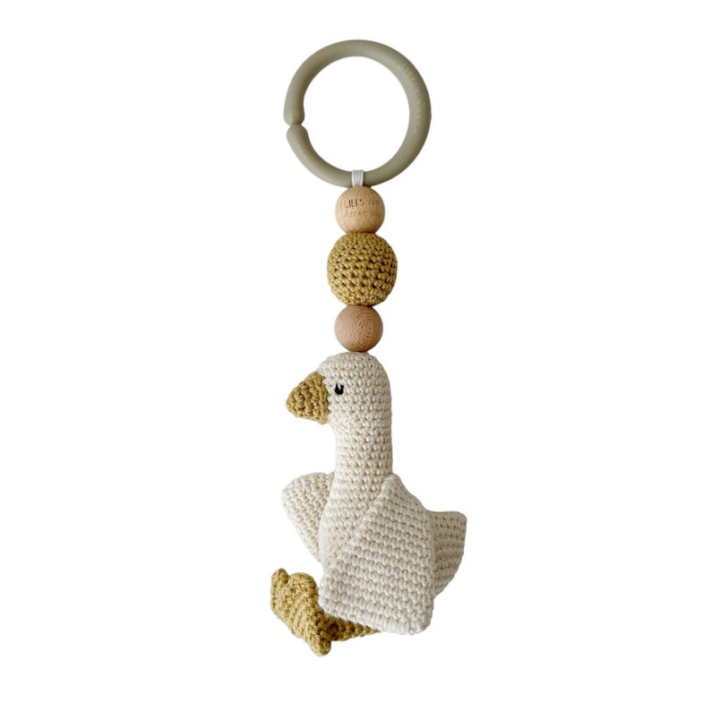 May include: A crocheted goose toy with a wooden ring and beads. The goose is white with yellow accents. The beads are natural wood and mustard yellow.