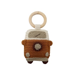 May include: A crocheted brown and beige toy van with a wooden ring attached. The van has a brown steering wheel and a white windscreen.
