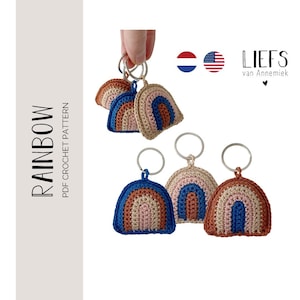 Op de afbeelding: Gehaakte regenboog sleutelhangers in blauw, bruin en roze. Elke sleutelhanger heeft een zilveren ring. De afbeelding bevat ook de tekst "RAINBOW PDF CROCHET PATTERN" en de merknaam "LIEFS van Annemiek".
