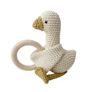 May include: A crocheted goose rattle toy with a wooden ring. The goose is white with a yellow beak and feet.