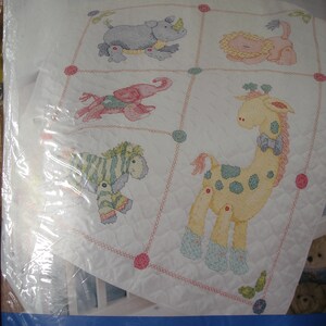 May include: A Bucilla Baby crib cover cross-stitch kit featuring a stamped design of jungle animals. The design includes a rhino, lion, elephant, giraffe, and zebra. The finished size is 34" x 43".