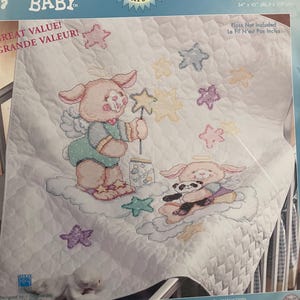 May include: A cross-stitch kit for a baby quilt featuring angel bunnies. The design includes two bunnies, stars, and the word "bubbles." The finished size is 34" x 43". The kit includes a free gift card.