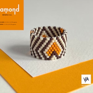 Könnte beinhalten: Ein brauner, weißer und goldener Perlenring mit geometrischem Muster. Der Ring ist in Peyote-Stich gearbeitet und hat einen Durchmesser von etwa 1,4 cm und einen Umfang von 6,4 cm.