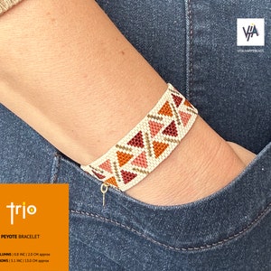 Pode incluir: Um bracelete branco de ponto peyote com um padrão geométrico em tons de marrom, rosa e laranja. O bracelete tem 2 polegadas de largura e 13 cm de comprimento. O bracelete é etiquetado como "trio" e "bracelete peyote".