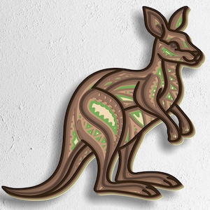Puede incluir: Escultura de canguro de madera en capas en tonos marrón, beige y verde, con intrincados patrones geométricos. El canguro se representa de perfil, de pie sobre sus patas traseras. La parte inferior de la imagen muestra el texto: SVG - EPS - DWG - DXF - AI.