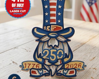 May include: A multi-layered laser-cut wooden gnome decoration featuring a tall top hat with stars and stripes, a beard, and a banner displaying the years 1776 and 2026. The centre of the gnome features the number 25, and the design uses red, white, and blue colours.