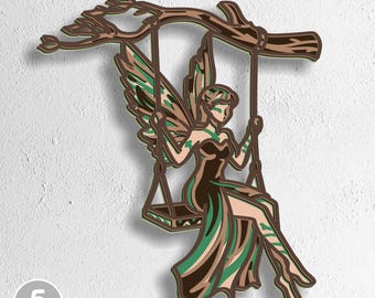 May include: A layered wooden art piece showing a fairy on a swing. The fairy wears a brown and green dress and has matching wings. The swing hangs from a tree branch. The artwork is labelled with "5 layers" and file type abbreviations.