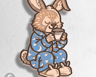 May include: A layered wooden artwork of a rabbit in blue pyjamas with a moon and star design, holding a mug. The rabbit wears bunny slippers. The artwork has a light brown and tan colour scheme. The text "6 LAYERS" and file type abbreviations are visible.