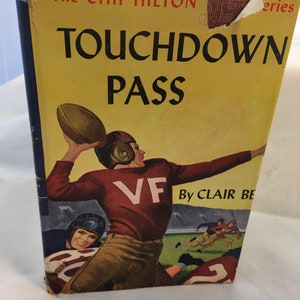 May include: Vintage book titled "Touchdown Pass" by Clair Bee, part of "The Chip Hilton" series. The cover features a football player in a maroon jersey throwing a football, with other players in the background. The book has a yellow background.