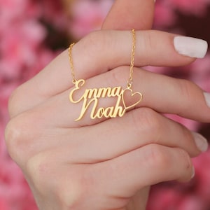 May include: Gold necklace with two names, "Emma" and "Noah", connected by a small heart charm.