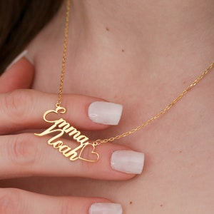 Puede incluir: Collar de oro con dos nombres, "Emma" y "Noah", unidos por un dije en forma de corazón.