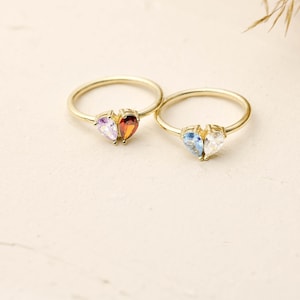 May include: Two gold rings with heart-shaped settings. One ring has a purple and orange gemstone, the other has a blue and clear gemstone.