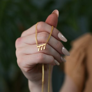 May include: A gold chain necklace with a pendant featuring the Hebrew letters for the number 777.