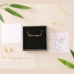May include: A gold necklace with the name "Candyn" written in cursive script. The necklace is displayed in a black box with a white card that says "by Lena art" and a website address.