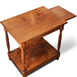 Könnte beinhalten: Ein Holz-Beistelltisch mit einer herunterklappbaren Ablage. Der Tisch ist aus dunklem Holz und hat ein schlichtes Design.