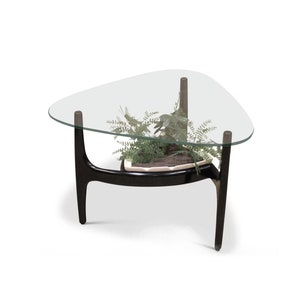 Könnte beinhalten: Ein dreieckiger Couchtisch mit einer Glasplatte und einem schwarzen Holzsockel und einem Regal. Eine Topfpflanze steht auf dem Regal.