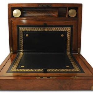 May include: A wooden writing desk with a leather writing surface and gold accents. The desk is open and the interior is visible. The desk has a hinged lid and a small drawer.