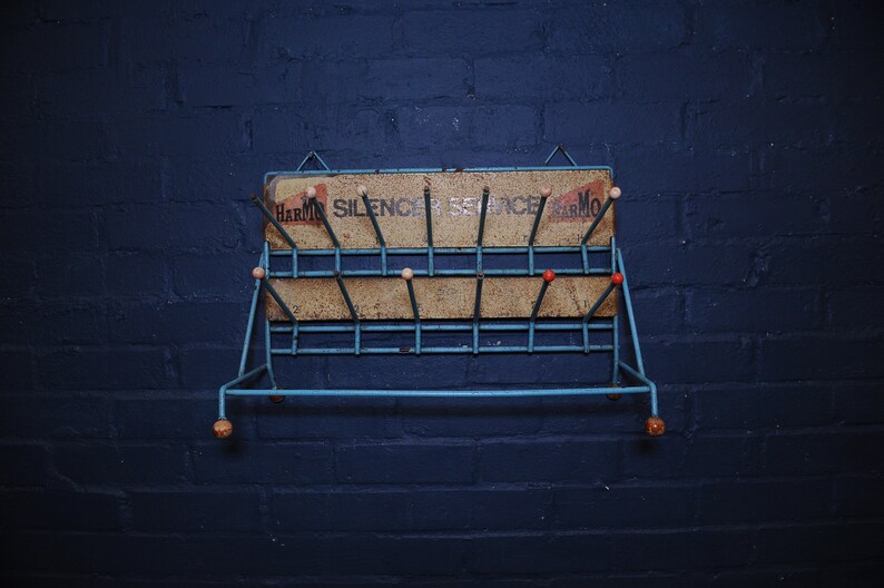 May include: A blue metal shoe rack with a sign that reads "Harmon Silencer Service Harmon". The rack has wooden knobs and is mounted on a blue brick wall.