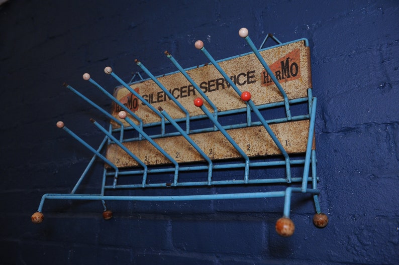 May include: A blue metal coat rack with a sign that reads "Harmo Silencer Service Harmo". The rack has 14 hooks with pink and red plastic tips.