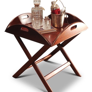 Può includere: Un tavolino da portata in legno marrone scuro con bordo curvo e maniglie ritagliate. Il vassoio contiene una caraffa di cristallo, due bicchieri, uno shaker per cocktail e un piccolo secchiello per il ghiaccio in metallo. Il tavolo ha una base a forma di X.