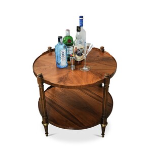 May include: A two-tiered round wooden side table with gold accents and a glass martini glass, four bottles of liquor, and a small metal jigger on the top tier.