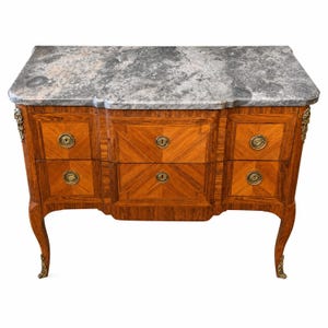 Può includere: Una cassettiera in legno con un piano in marmo grigio dal bordo ondulato. Il mobile presenta quattro cassetti disposti su due file, decorati con motivi geometrici in impiallacciatura di legno, pomelli circolari in ottone e fregi in ottone.