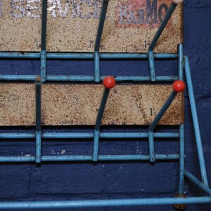 May include: A blue metal shoe rack with red and white knobs. The rack is mounted on a blue wall and has a rusty metal back.