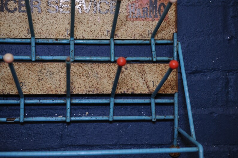 May include: A blue metal shoe rack with red and white knobs. The rack is mounted on a blue wall and has a rusty metal back.