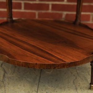 May include: A round wooden table with a dark brown finish and gold accents. The table has a scalloped edge and sits on four legs.