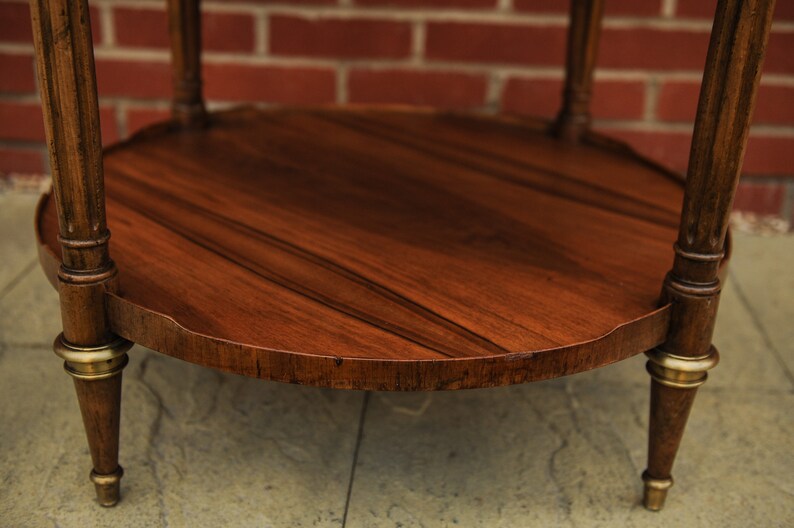 May include: A round wooden table with a dark brown finish and gold accents. The table has a scalloped edge and sits on four legs.