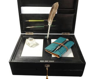 Op de afbeelding: Een zwarte houten schrijfkist met een messing slot en sleutel. De kist is open en bevat een klein notitieboekje, een glazen inktpot en een pen.