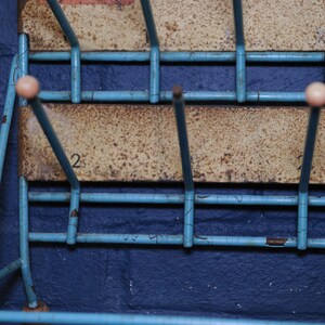 May include: A blue metal shoe rack with white plastic knobs. The rack has two shelves and is mounted on a wall. The number "2" is visible on the top shelf.