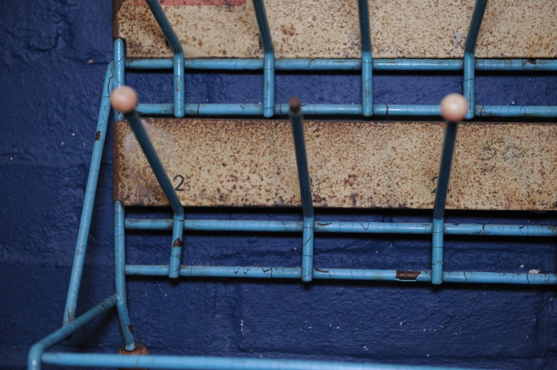 May include: A blue metal shoe rack with white plastic knobs. The rack has two shelves and is mounted on a wall. The number "2" is visible on the top shelf.