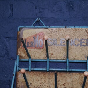May include: A blue metal rack with a sign that reads "Marmo Silencer Service". The rack has several metal rods with white plastic tips.