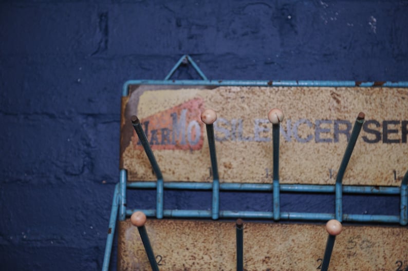 May include: A blue metal rack with a sign that reads "Marmo Silencer Service". The rack has several metal rods with white plastic tips.