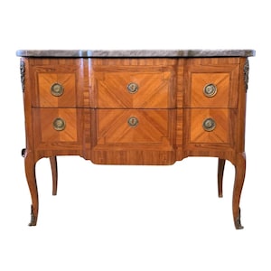 May include: A wooden chest of drawers with a marble top. The chest has a geometric pattern on the drawers and brass hardware. The legs are curved. The chest is approximately 40 inches wide.