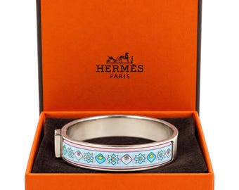 May include: A silver-toned hinged bangle bracelet featuring a light blue enamel inlay with a repeating pattern of stylized flowers and geometric shapes, presented inside an orange box with the text HERMES PARIS printed on the lid.