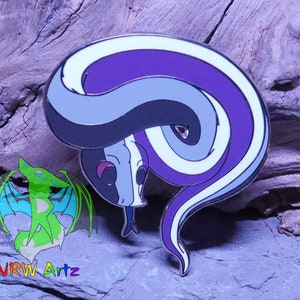 May include: A purple, white and black enamel pin of a curled up snake with a white stripe down its back. The snake is curled up in a circle with its head tucked in. The pin is on a wooden background.