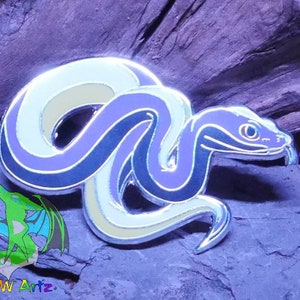 May include: A silver enamel pin featuring a purple, black, and white snake curled up. The snake has a black eye and a white tongue.