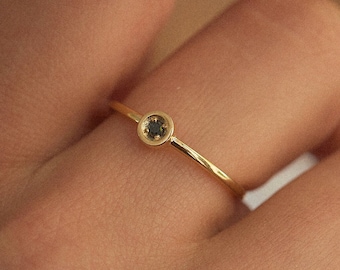 May include: A delicate gold ring with a small, round, black gemstone set in the center.