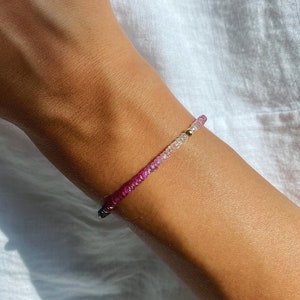 Op de afbeelding: Een armband met een gradiënt van roze, paarse en witte edelstenen. De armband is gemaakt van kleine, ronde kralen en wordt om de pols gedragen.