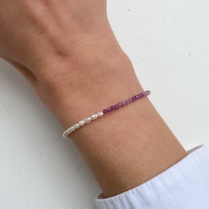 Peut inclure: Un bracelet délicat avec des perles blanches et des pierres précieuses violettes. Le bracelet est porté au poignet.